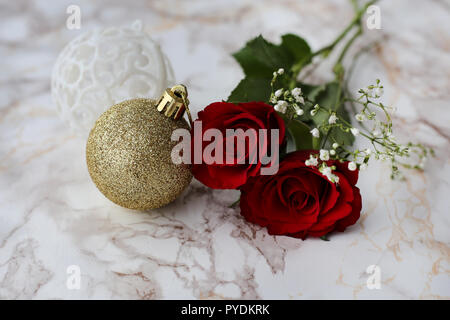 Red and white flowers with beautiful glittery Christmas ornaments. Photographed on a white marble surface. A still life photo with Christmas theme. Stock Photo