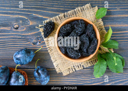 Prunes in a clay bowl and fresh plums, leaves on a wooden table. Fresh prunes for healthy life.
