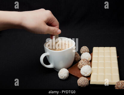 Woman adding sugar in coffee in cafe. Cofe, Stack of Black and White Chocolate isolated on black background, place for text. Stock Photo