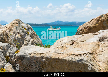 Rocks on the beach natural framing turquoise seascape woth a small speed boat in the center of the image and many other small islands in backgound, on Stock Photo