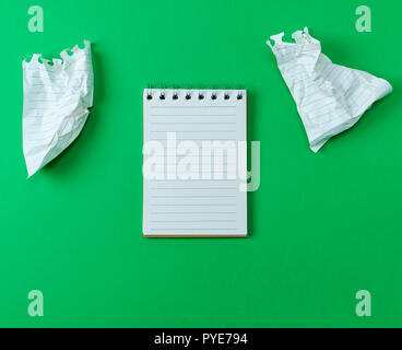 open small blank notebook with white sheets on a green background, next to two crumpled sheets Stock Photo