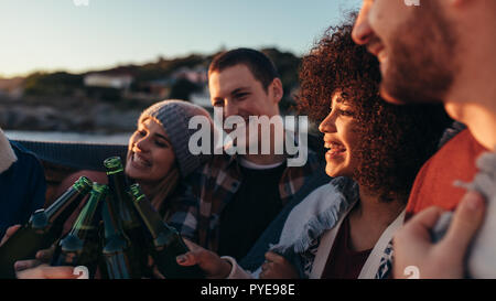 Group of friends having party celebrating and drinking at the beach in evening. Multiracial young people toasting beer bottles at the beach. Stock Photo