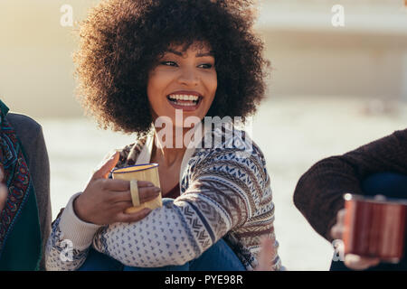 Beautiful young woman sitting at the beach with friends having coffee. Group of friends having coffee at beach. Stock Photo