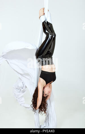 Young woman doing tricks on a white canvases. She hangs upside down. Stock Photo