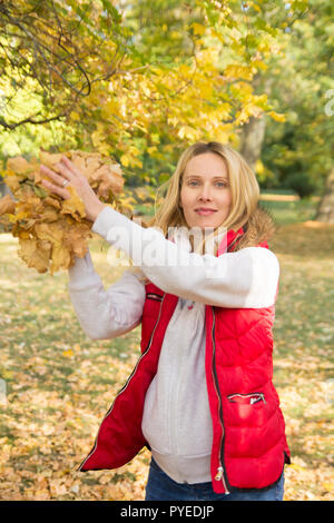 cheerful young woman throwing leaves in autumn forest Stock Photo