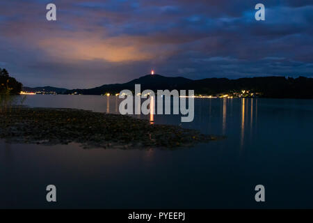 colored clouds over lake with a pier in the middle and reflection in the water. Captured on Woerthersee, Kaernten, Austria. Stock Photo