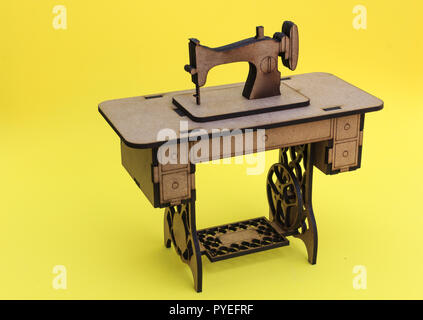 Mini sewing machine, made of wood, on yellow background. Stock Photo