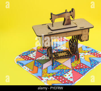 Mini sewing machine, made of wood, on a patchwork rug, with yellow background. Stock Photo