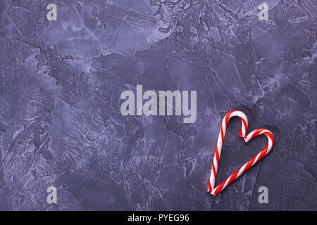 Christmas candy canes lie on a dark concrete background in the shape of a heart with copy space. Stock Photo