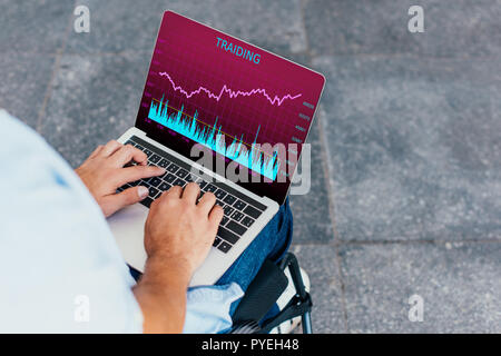 cropped image of man in wheelchair using laptop with traiding appliance on street Stock Photo