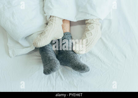 cropped shot of couple in woolen socks lying in bed together at home Stock Photo