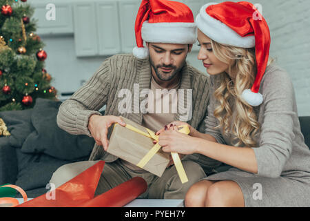focused young couple in santa hats decorating christmas gift together at home Stock Photo