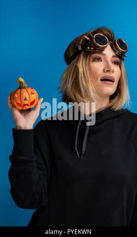 Portrait of steam punk girl holding up a carved Halloween pumpkin. Female hip-hop goth fashion Stock Photo