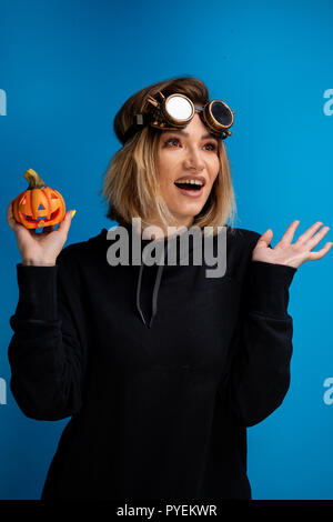 Portrait of steam punk girl wearing a black hoodie holding up a carved Halloween pumpkin. Posing witch craft themed photoshoot Stock Photo