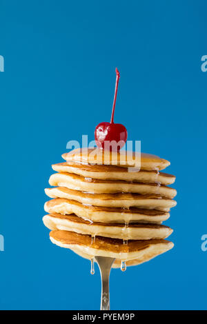 Stack of pancakes with honey decorated sweet cherry pinned on a fork on blue background Stock Photo