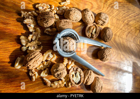 Walnut kernels and whole walnuts  with a nutcracker on wooden table Stock Photo