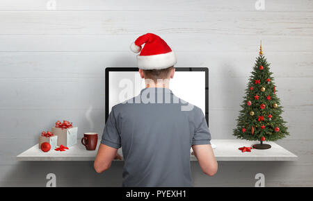 Man working in office with Santa Claus hat. Christmas tree and gifts beside. Copy space on left side. Stock Photo
