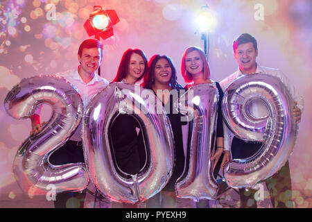 New Year party concept. Group of young friends holding silver colored numbers 2019 and throwing confetti Stock Photo