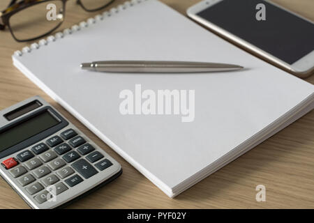 Notepad, calculator, smartphone, glasses and sliver ballpen on wooden office desk. Image with copy space. Selective focus. Stock Photo