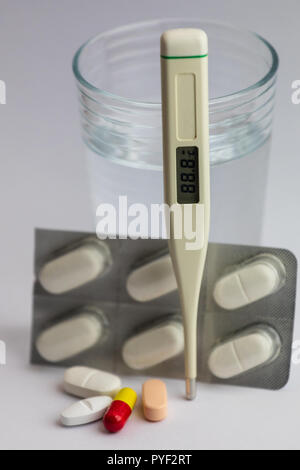 pills in different colors, a blister pack, a thermometer and a glass of water on white background, medicine Stock Photo