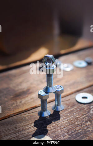 A figure of one small robot assembled from several bolts and nuts standing in a vertical position on a table made of planks. It symbolizes technology, Stock Photo
