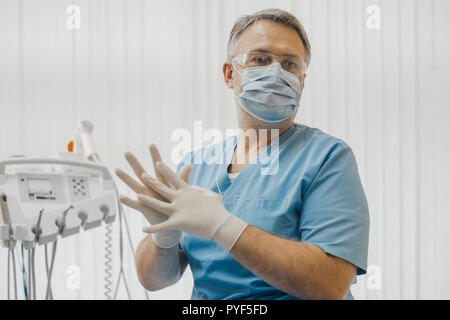 Man dentist sitting next to dental equipment and putting on latex gloves. Stock Photo