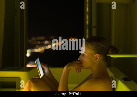 woman in hotel bathroom reading on tablet, Santorini, Greece Stock Photo