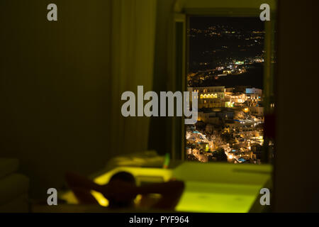 woman in the bathroom at the hotel enjoying the view of the night city, Santorini, Greece Stock Photo