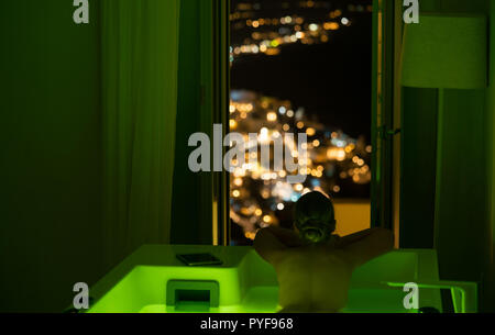 woman in the bathroom at the hotel enjoying the view of the night city, Santorini, Greece Stock Photo