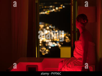 woman in the bathroom at the hotel enjoying the view of the night city, Santorini, Greece Stock Photo