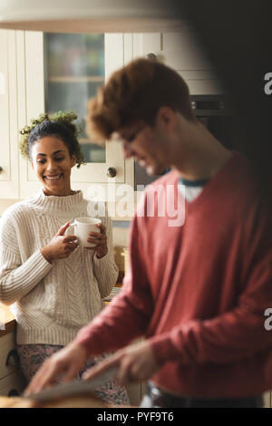 Woman having coffee while man cutting loaf of bread in kitchen Stock Photo