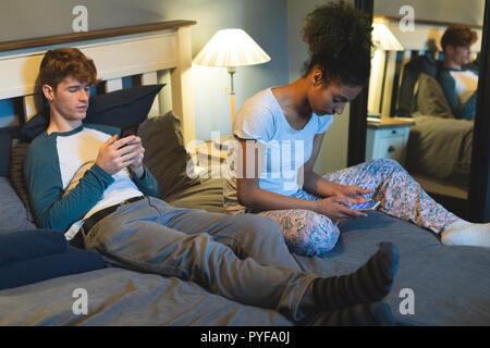 Couple using mobile phones in bedroom Stock Photo