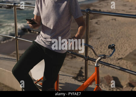 Man with bicycle using mobile phone near railing at beach Stock Photo