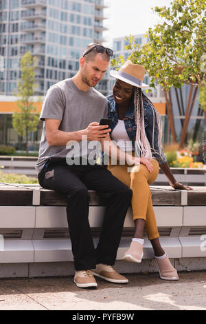 Smiling couple sitting on the bench and using mobile phone Stock Photo