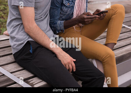 Couple sitting on the bench using mobile phone Stock Photo