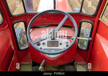 The tractor rides in the field, looking from the inside. The interior of the red retro tractor with steering wheel and dashboard. Stock Photo