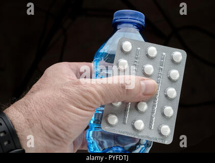 Man holds with left hand a bottle of water and a pill bottle Stock Photo
