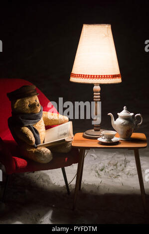 Surreal scene with a teddy bear - in the garden winter time a little living room - red chair, table and lamp and tea service set - waiting for Santa C Stock Photo