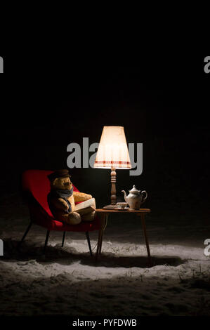 Surreal scene with a teddy bear - in the garden winter time a little living room - red chair, table and lamp and tea service set - waiting for Santa C Stock Photo