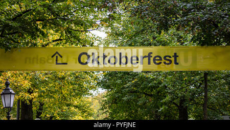 Oktoberfest, Bavaria, Germany. Entrance to the fairground, yellow informative sign, text oktoberfest, green trees background Stock Photo