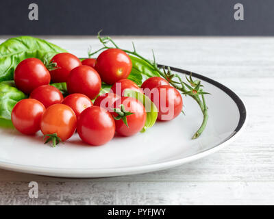 Cherry Tomatoes With an Empty Vine and Basil Leaves on a White Plate Stock Photo