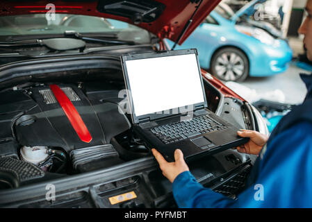 Engineer with laptop makes computer diagnostics of the car engine in auto-service. Vehicle wiring inspection Stock Photo