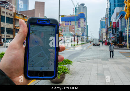 A male hand holding a smartphone, using Google Maps to navigate around Haeundae, part of Busan in South Korea. Stock Photo