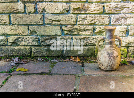 Dirty yellow brick wall with a old historical looking urn and stone pavements background texture Stock Photo
