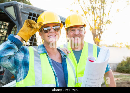 Male and Female Workers With Technical Blueprints at Construction Site Stock Photo