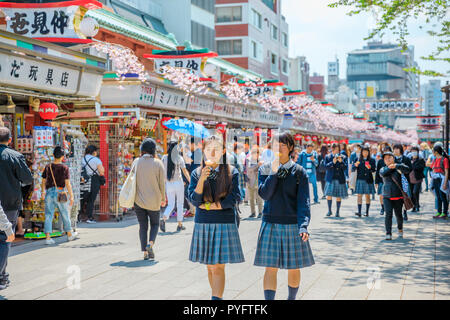 Tokyo, Japan - April 19, 2017: young teens in school uniforms walking on Nakamise Dori, street with food and souvenirs shops, eating an ice cream. Kaminarimon Gate of Sensoji Temple on background. Stock Photo
