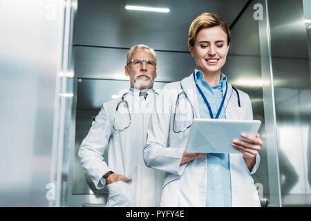 happy female doctor using digital tablet while her male colleague standing behind in elevator Stock Photo