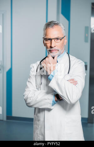 thoughtful middle aged male doctor with stethoscope over neck looking at camera in hospital Stock Photo