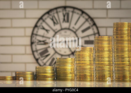 stacks of gold coins step over the vintage clock on the wall background, investment and financial concept Stock Photo