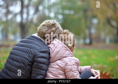 Woman and young girl, teenager, mother and her daughter sit in the park, close o each other, lifestyle close to nature. Stock Photo